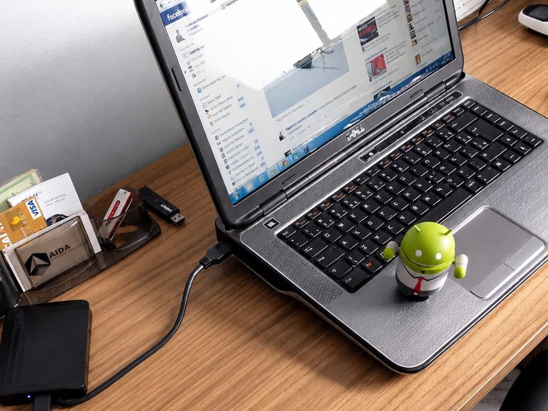 Notebook aberto em uma rede social, ao lado de um boneco do Android